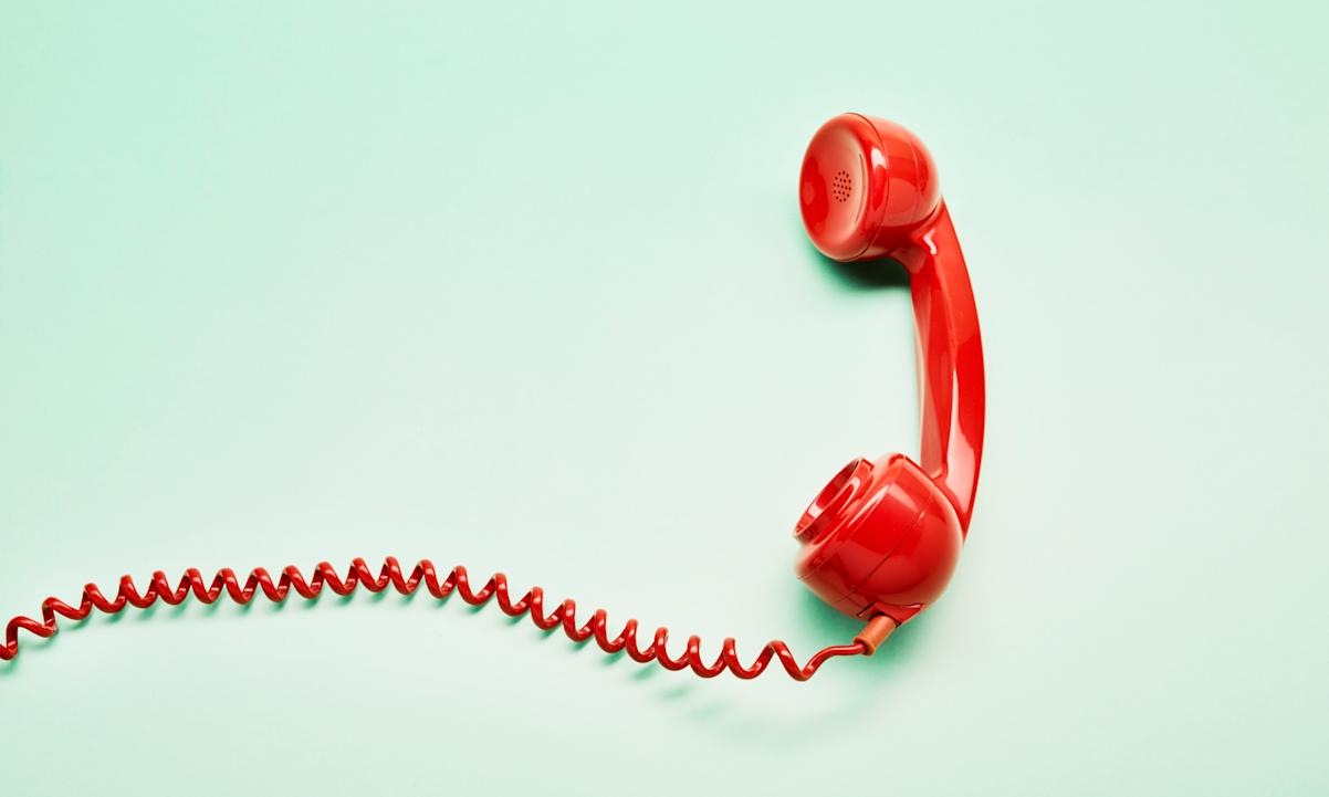 High angle view of a red old-fashioned telephone receiver with a coiled cable on turquoise background - stock photo