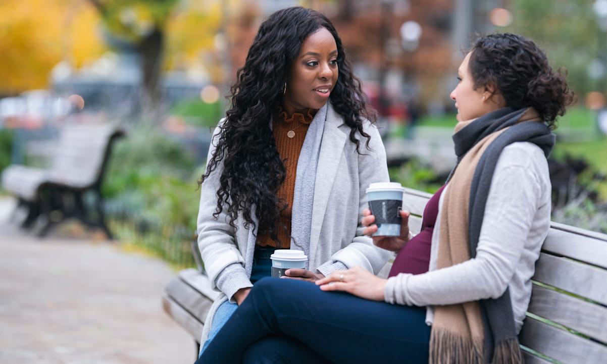 Two female friends have a conversation on a park bench